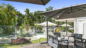 Eine Holzterrasse mit Gartenmöbeln, einem Pool und einem tropischen Garten.