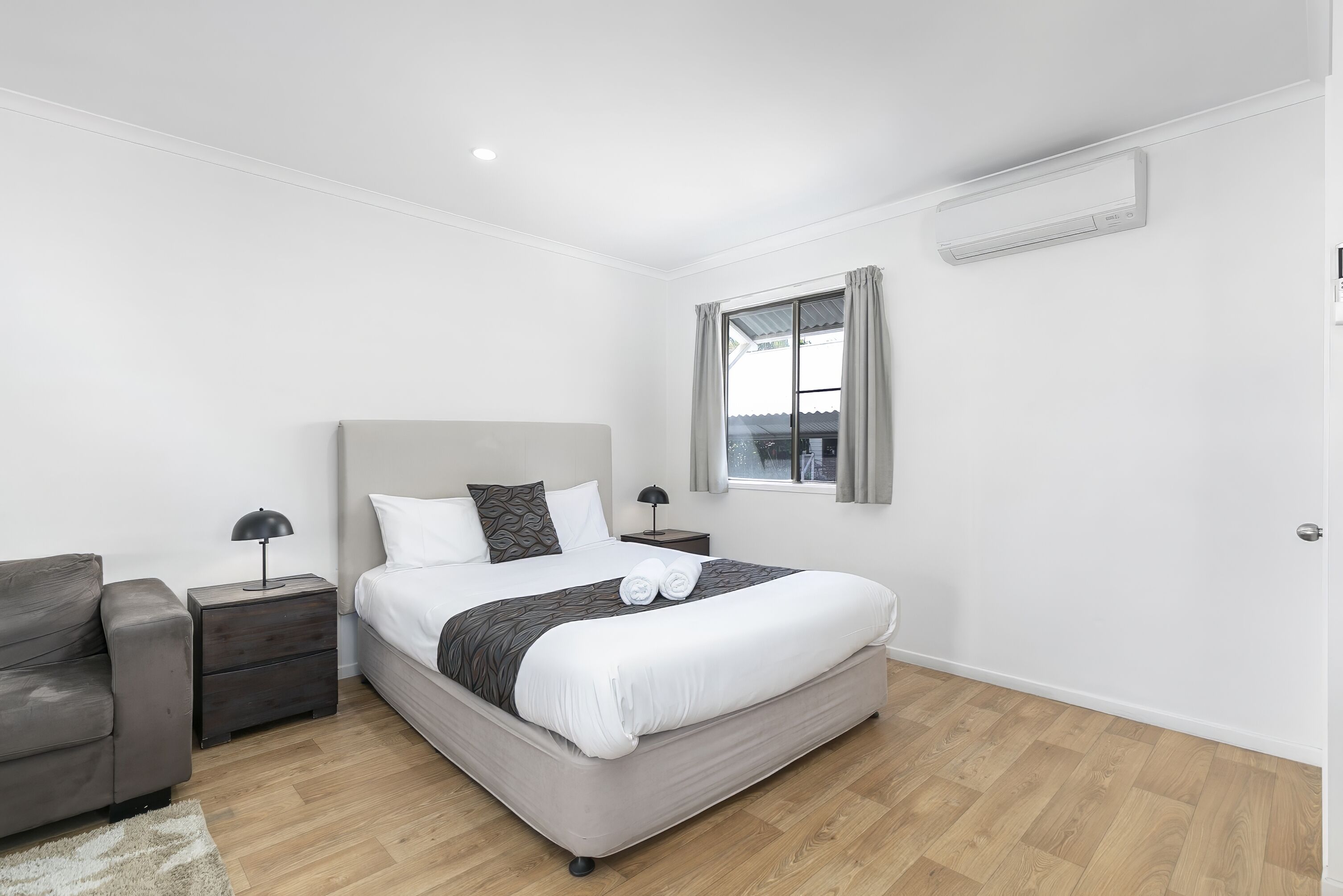 A modern bedroom with a bed, a nightstand, a lamp, a chair, and a window with curtains.