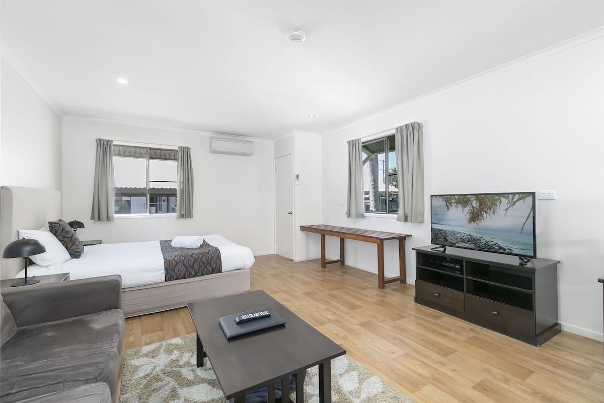 A modern hotel room with a bed, a sofa, a desk, a TV, and a window with curtains.