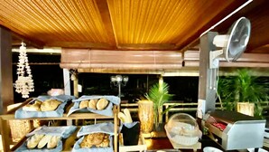 A bakery counter with bread and pastries displayed on shelves, a fan, and a coffee machine. - De Baron Resort (Langkawi)