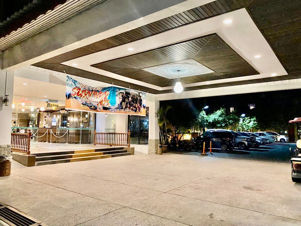 A modern building entrance with a 'Welcome' sign, a bar, and a parking area.