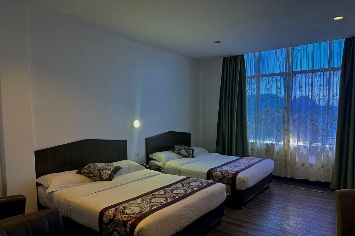 A hotel room with two beds, a wooden floor, a large window with curtains, and a night light.
