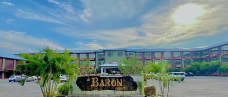 Entrada a un resort con un cartel que dice "de BARON Resort", rodeada de palmeras y un estacionamiento.