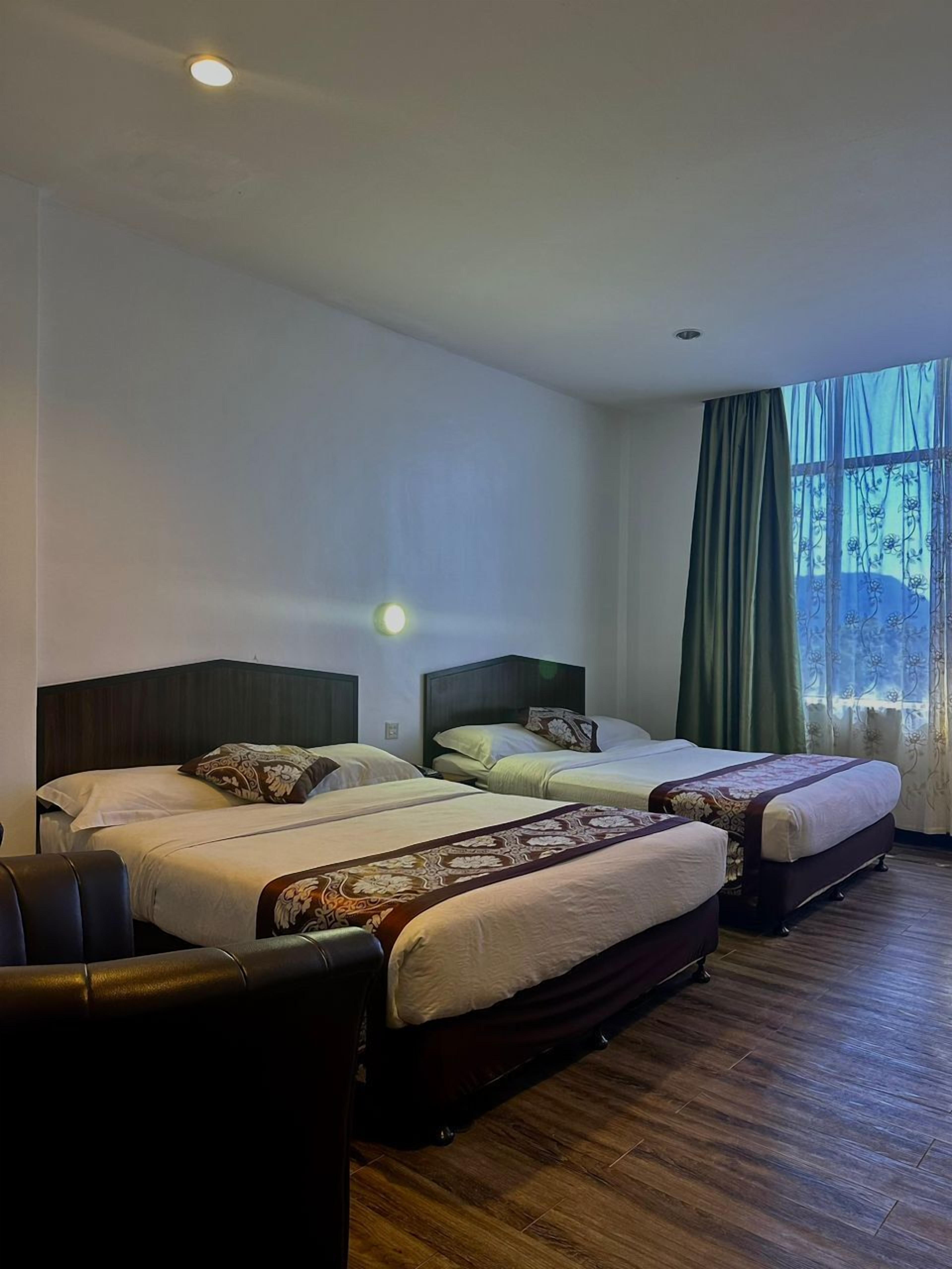A hotel room with three beds, a wooden floor, and a large window with curtains.