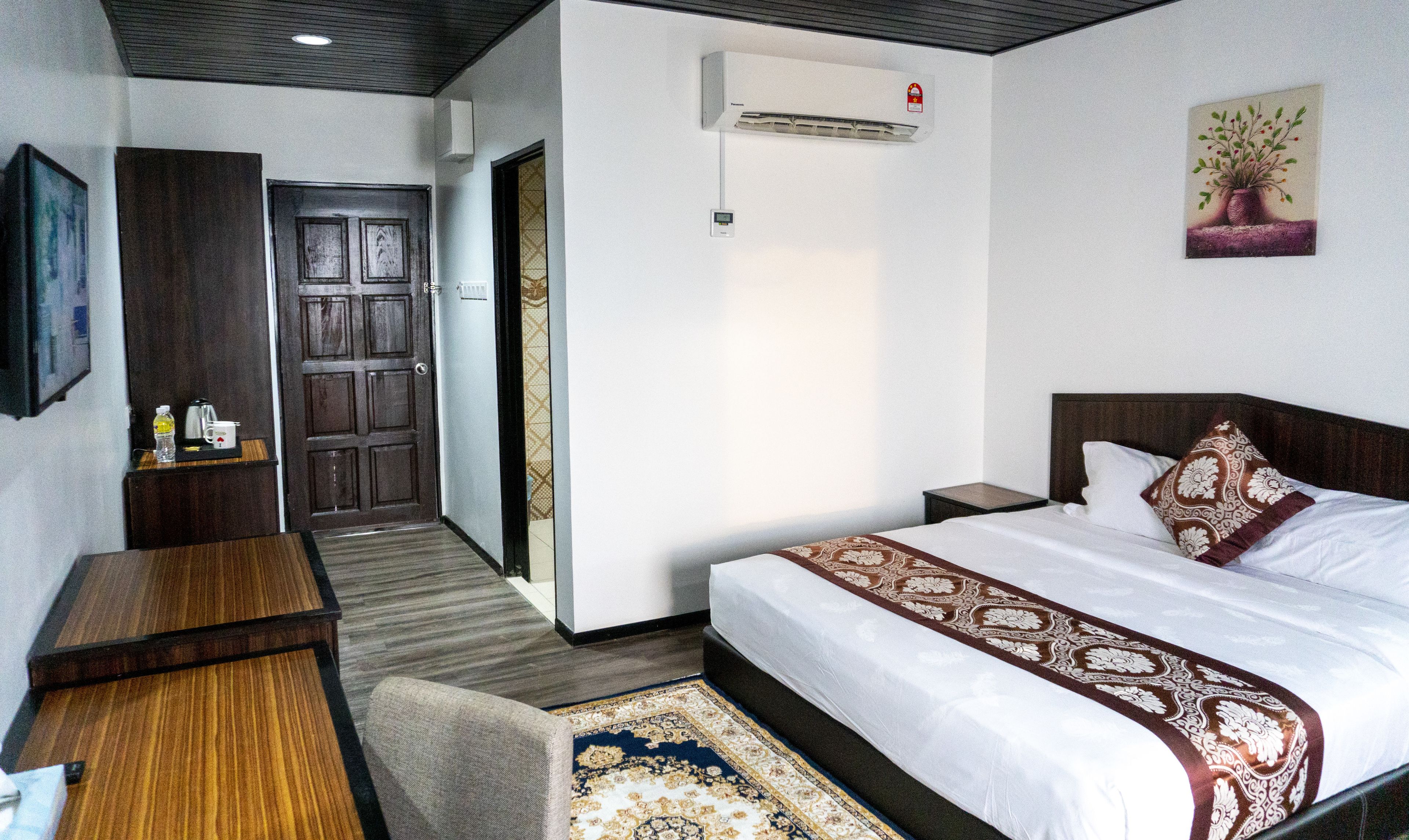 Habitación de hotel con cama, mesita de noche y escritorio. Se ve una puerta que da a otra habitación y un equipo de aire acondicionado en la pared.