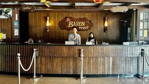 A reception desk at De Baron Resort with a wooden backdrop, two receptionists, and a sign indicating 'Cashier' and 'Reception' areas. - De Baron Resort (Langkawi)
