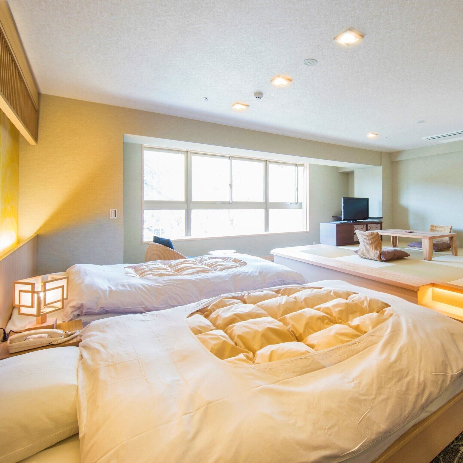 Habitación de hotel con dos camas, televisión, escritorio y ventana grande.