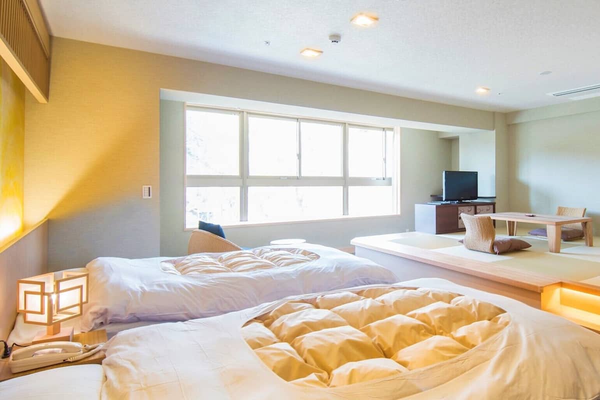 A hotel room with two beds, a TV, a desk, and a large window.