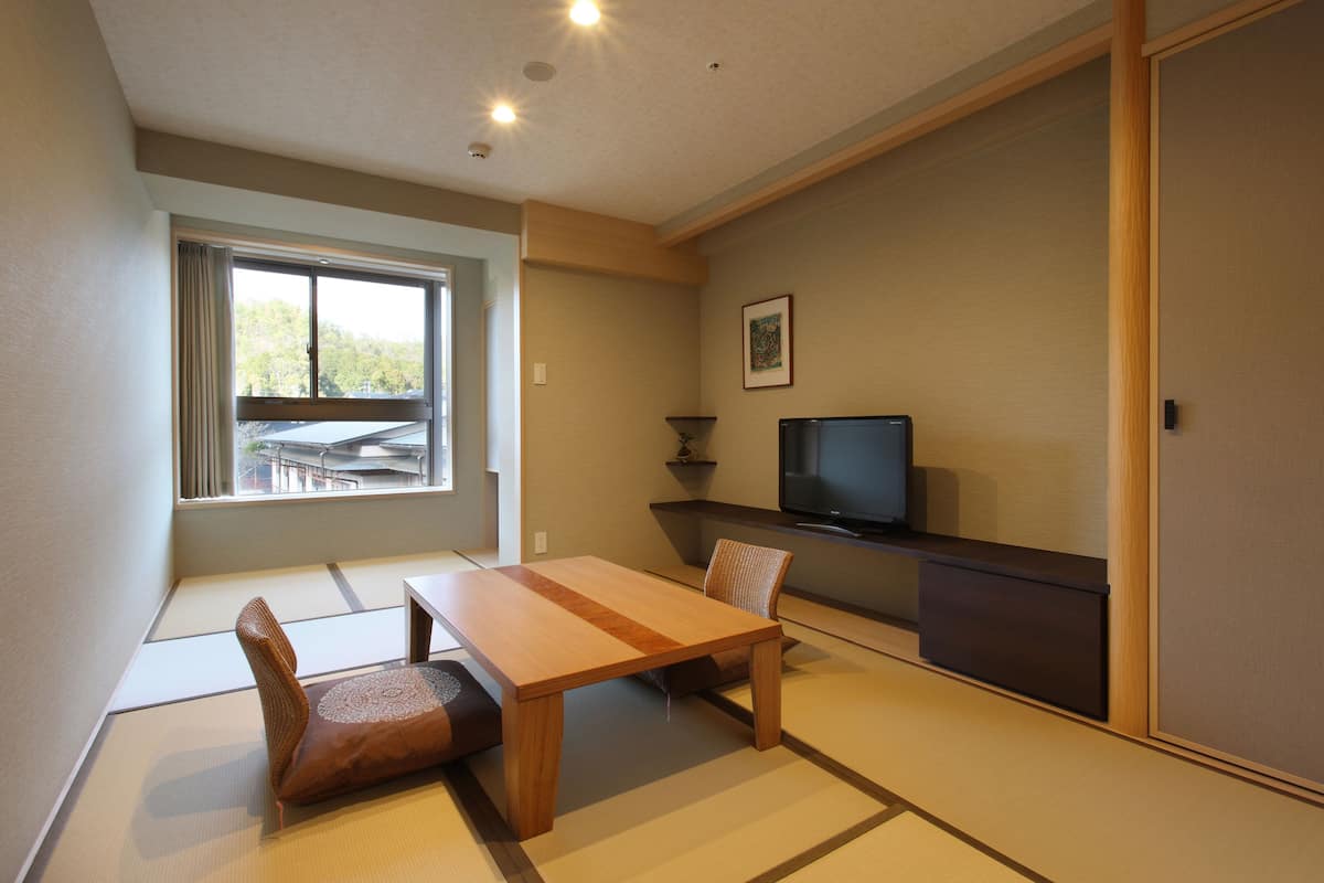 A traditional Japanese room with tatami flooring, a low wooden table, and a television on a stand.