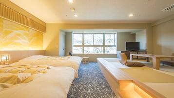 Habitación de hotel con dos camas, un televisor, una mesita y una ventana que da a árboles.