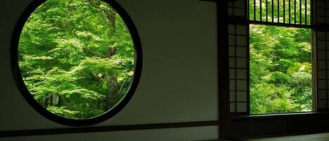 Um quarto japonês tradicional com piso de tatame, um painel shoji e uma janela redonda com vista para uma floresta verdejante.