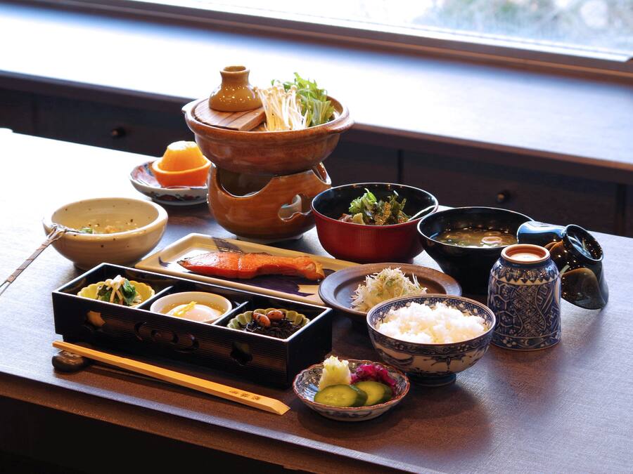 Una comida tradicional japonesa con diversos platos y utensilios sobre una mesa de madera.