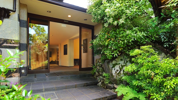 A stone staircase leading to a building entrance, surrounded by lush greenery and a rock wall. - Ryokan Nenrinbo (Kyoto)