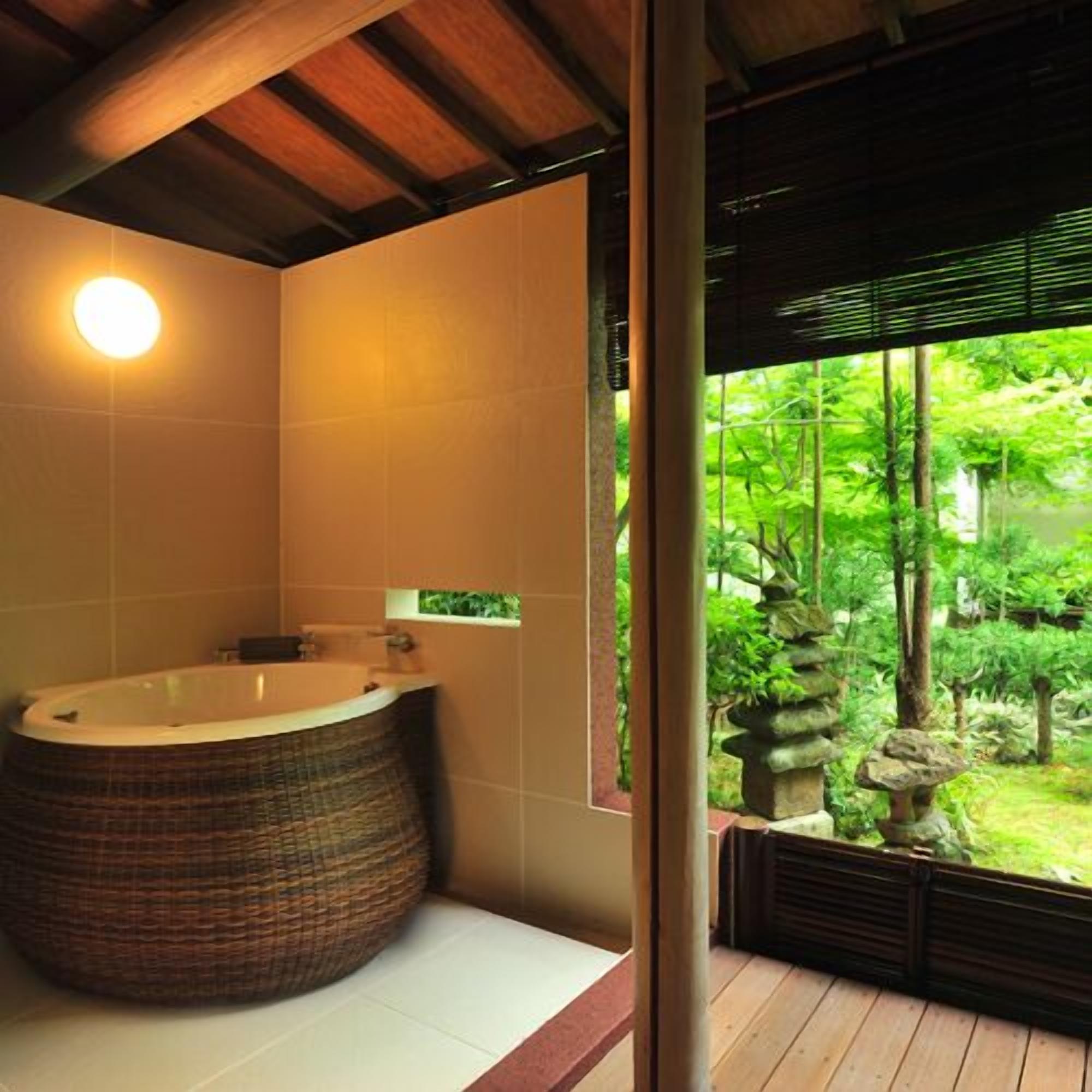 A bathroom with a large bathtub, a window with a view of greenery, and a wooden ceiling.