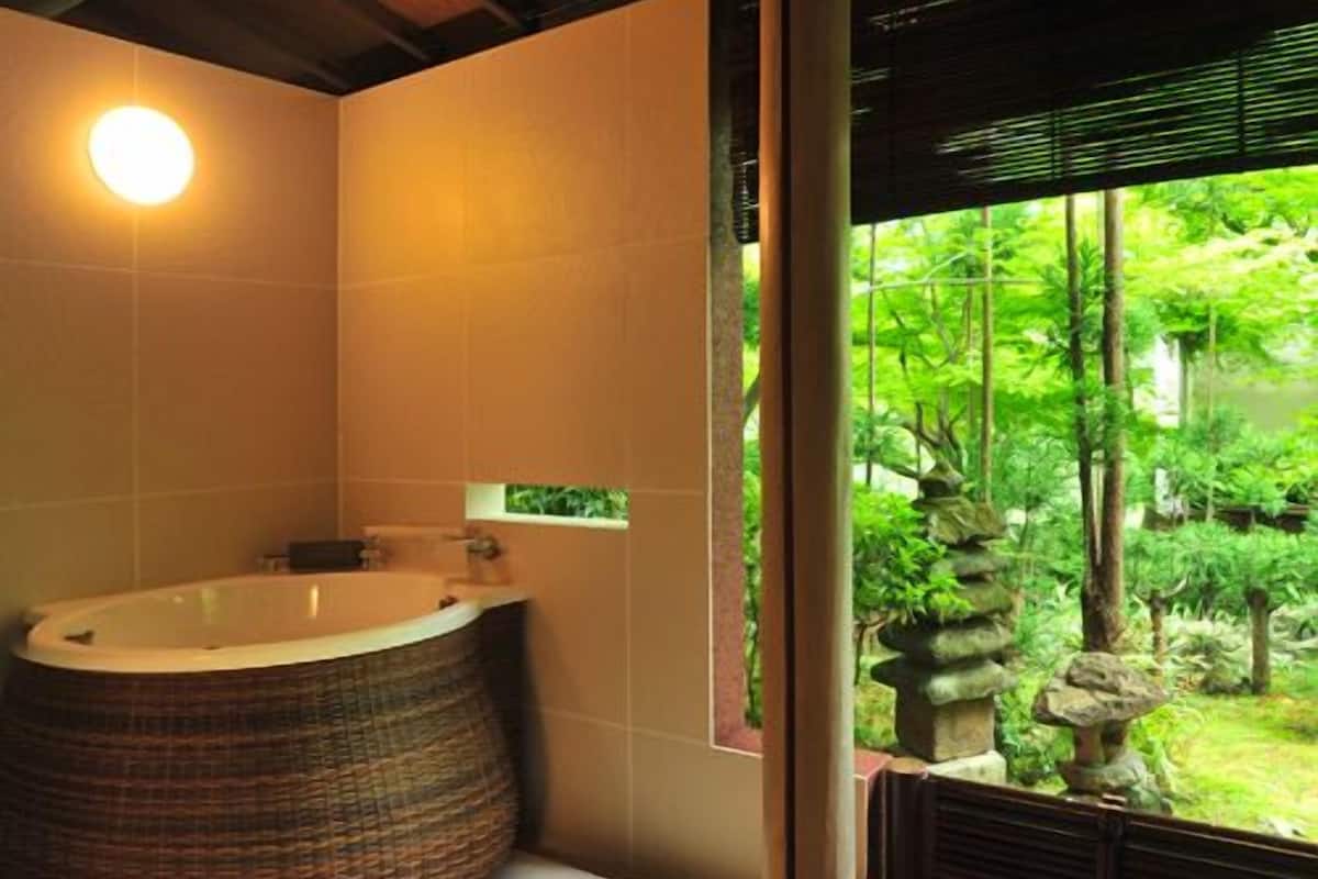 A bathroom with a large bathtub, a window with a view of greenery, and a wooden ceiling.