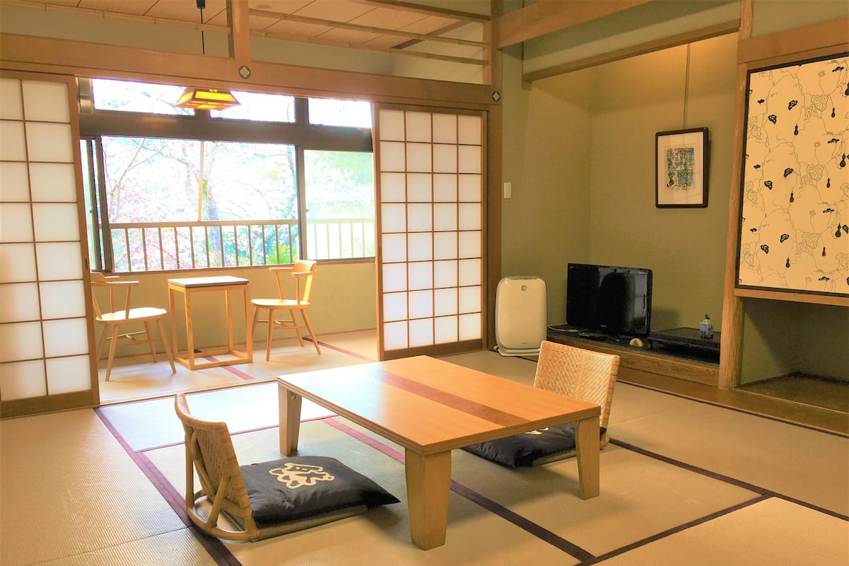 A traditional Japanese room with tatami flooring, a low table, two chairs, a television, and a framed map on the wall.