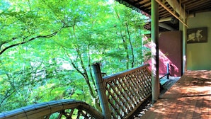 A covered wooden deck with a bamboo fence overlooking a lush green forest. - Ryokan Nenrinbo (Kyoto)