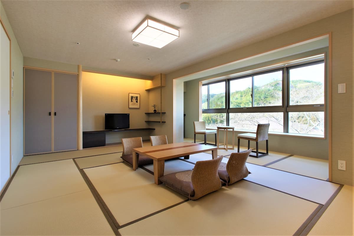 A traditional Japanese room with tatami flooring, a low table, cushions, and a TV.