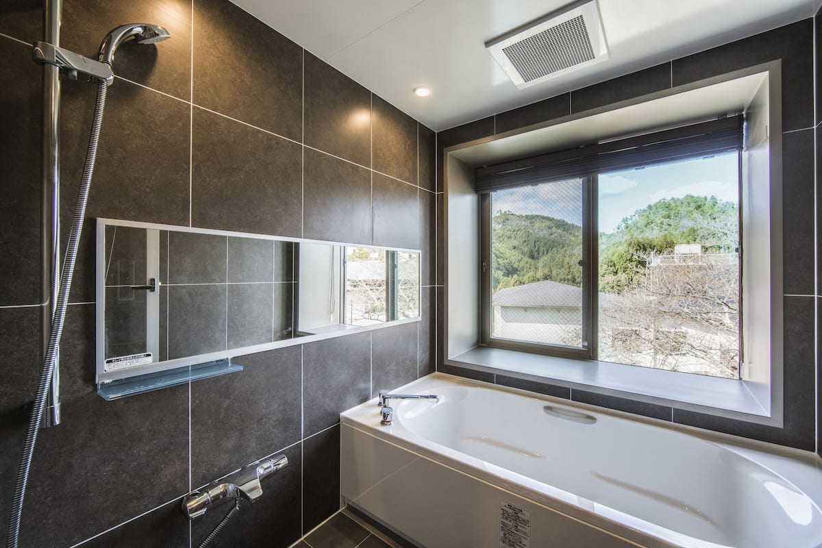 A modern bathroom with a bathtub, a shower, and a window providing a view of the outdoors.
