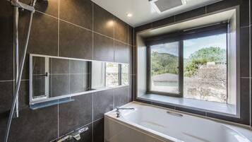 A modern bathroom with a bathtub, a shower, and a window providing a view of the outdoors.