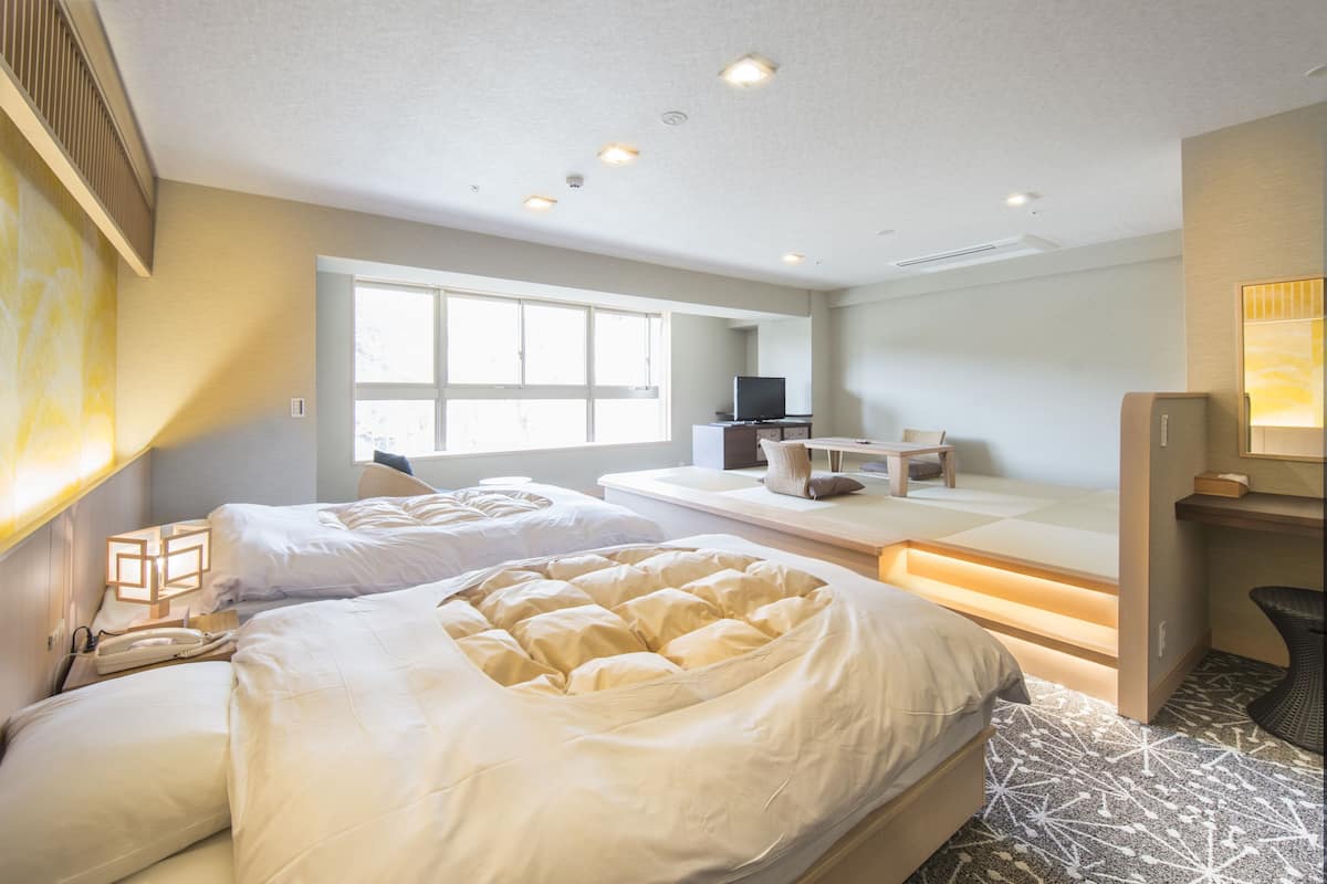 A hotel room with two beds, a desk, a chair, and a television.