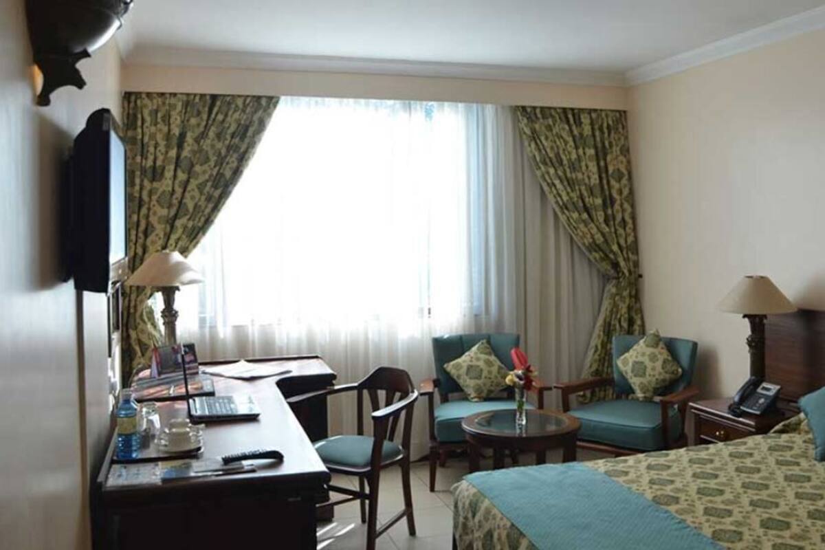 A hotel room with a bed, two chairs, a desk with a computer, a lamp, and a telephone.