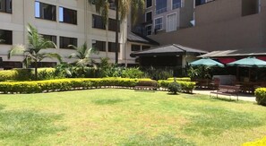 A courtyard with a lawn, palm trees, and a covered seating area with umbrellas. - Jacaranda (Nairobi)