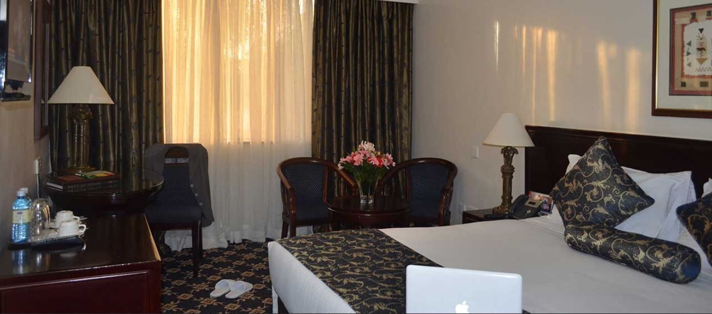A hotel room with a bed, two chairs, a desk with a lamp, a laptop, and a vase with flowers.
