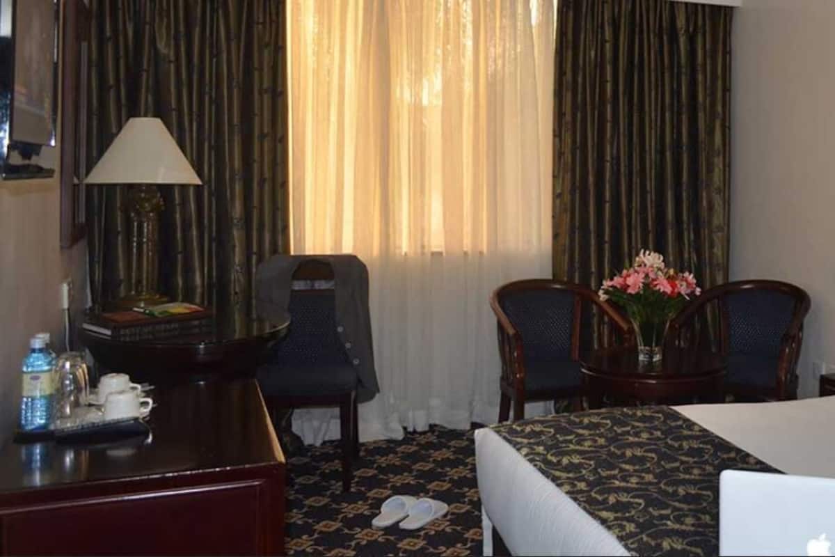 A hotel room with a bed, two chairs, a desk, a laptop, and a lamp.
