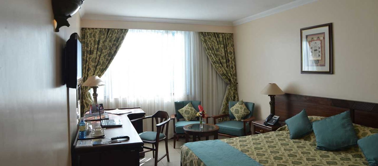 A hotel room with a bed, two chairs, a desk with a computer, a lamp, and a telephone.