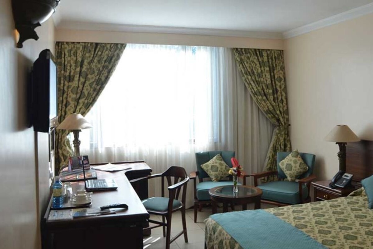 A hotel room with a bed, two chairs, a desk with a computer, a lamp, and a telephone.