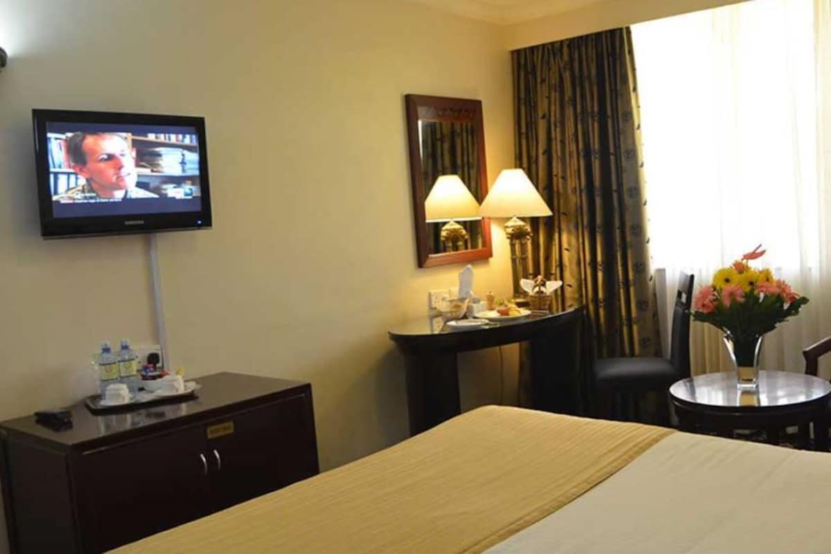 Habitación de hotel con cama, escritorio, silla, televisor y ventana con cortinas.