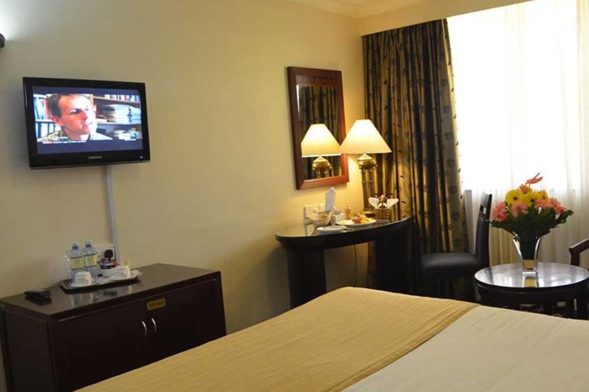 A hotel room with a bed, a desk, a chair, a TV, and a window with curtains.