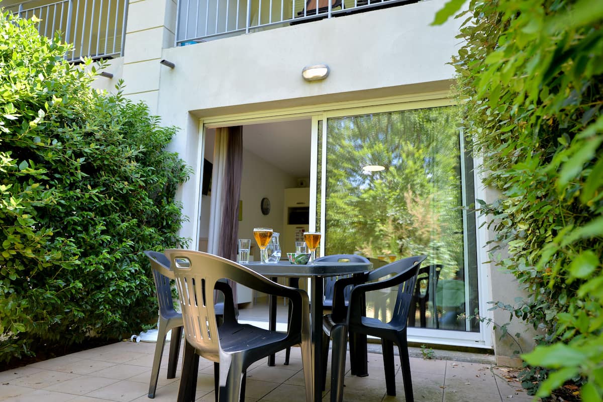 An outdoor patio with a table and chairs, surrounded by greenery.