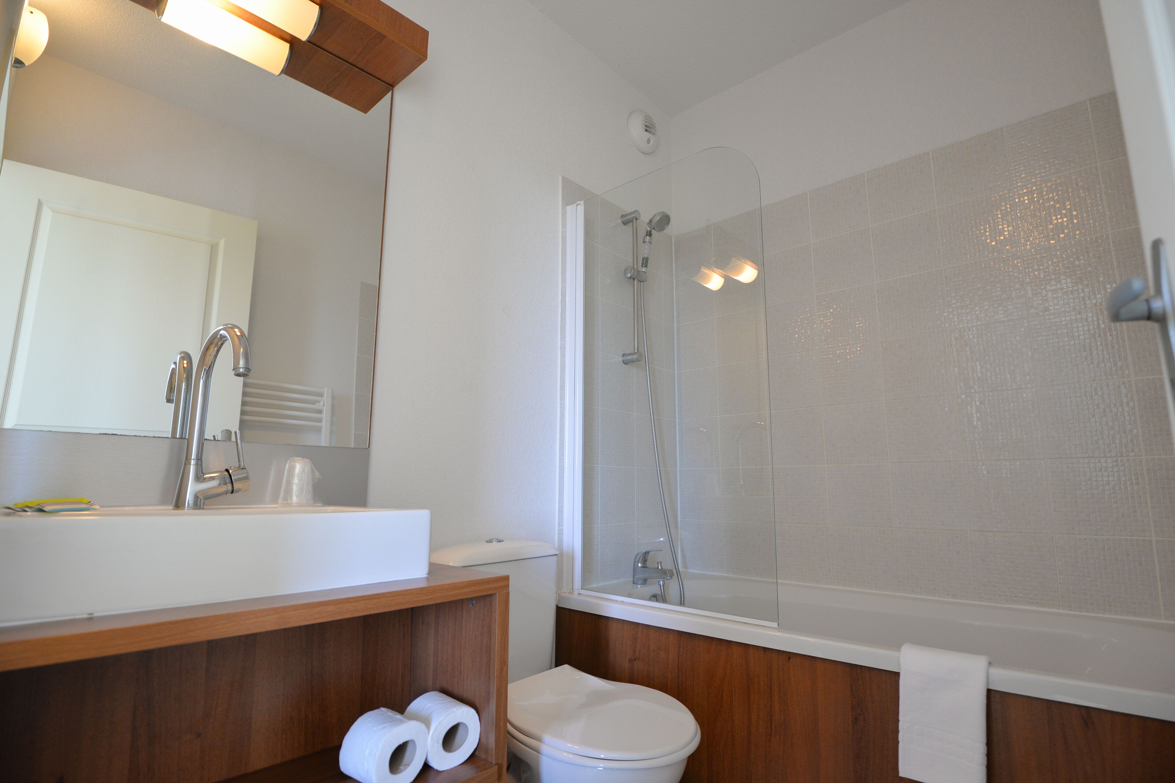 A bathroom with a white sink, mirror, wooden vanity, toilet, and a glass-enclosed shower area.