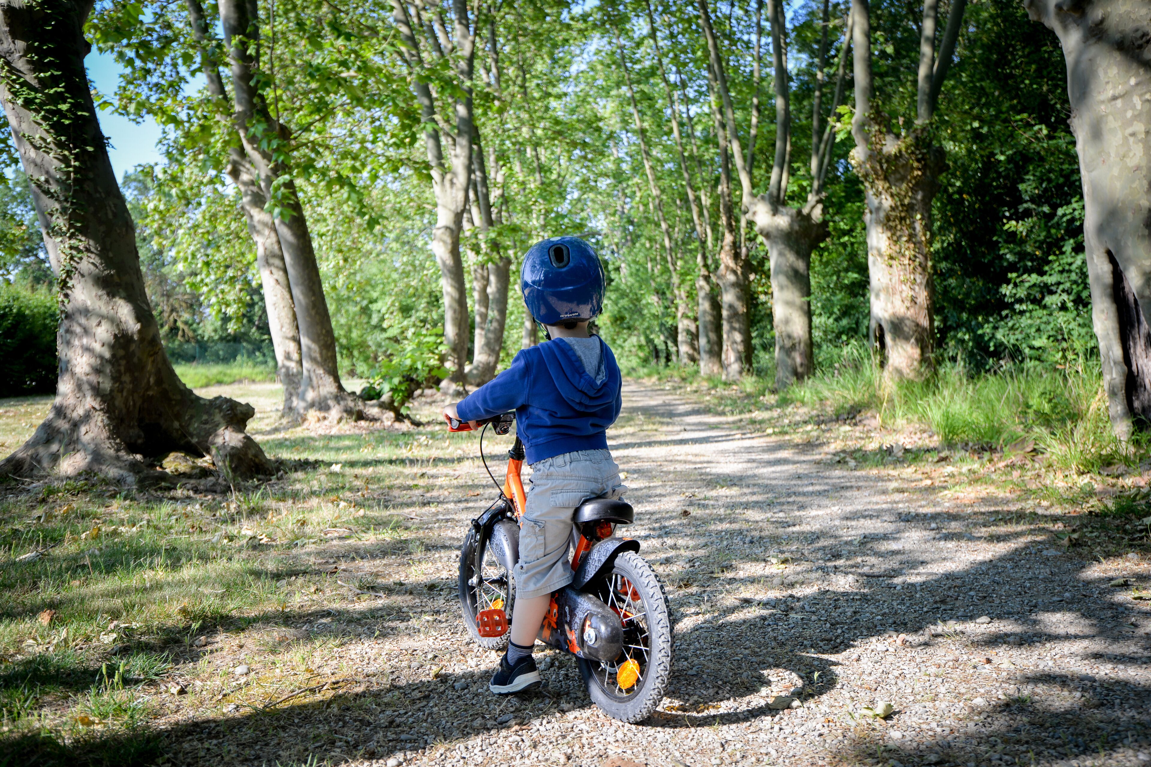A child riding a bicycle on a gravel path surrounded by trees.
