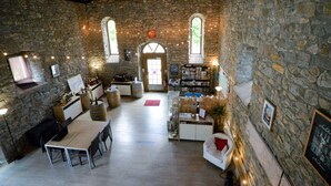Una habitación rústica con paredes de piedra y techo de madera, un comedor con mesa y sillas, una zona de bar con botellas y vasos, y un rincón de estar acogedor con un sofá y una almohada roja.