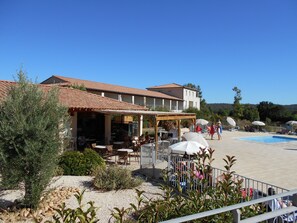 Un complexe hôtelier doté d’une terrasse, d’une piscine et d’un bâtiment dont le toit est recouvert de tuiles.