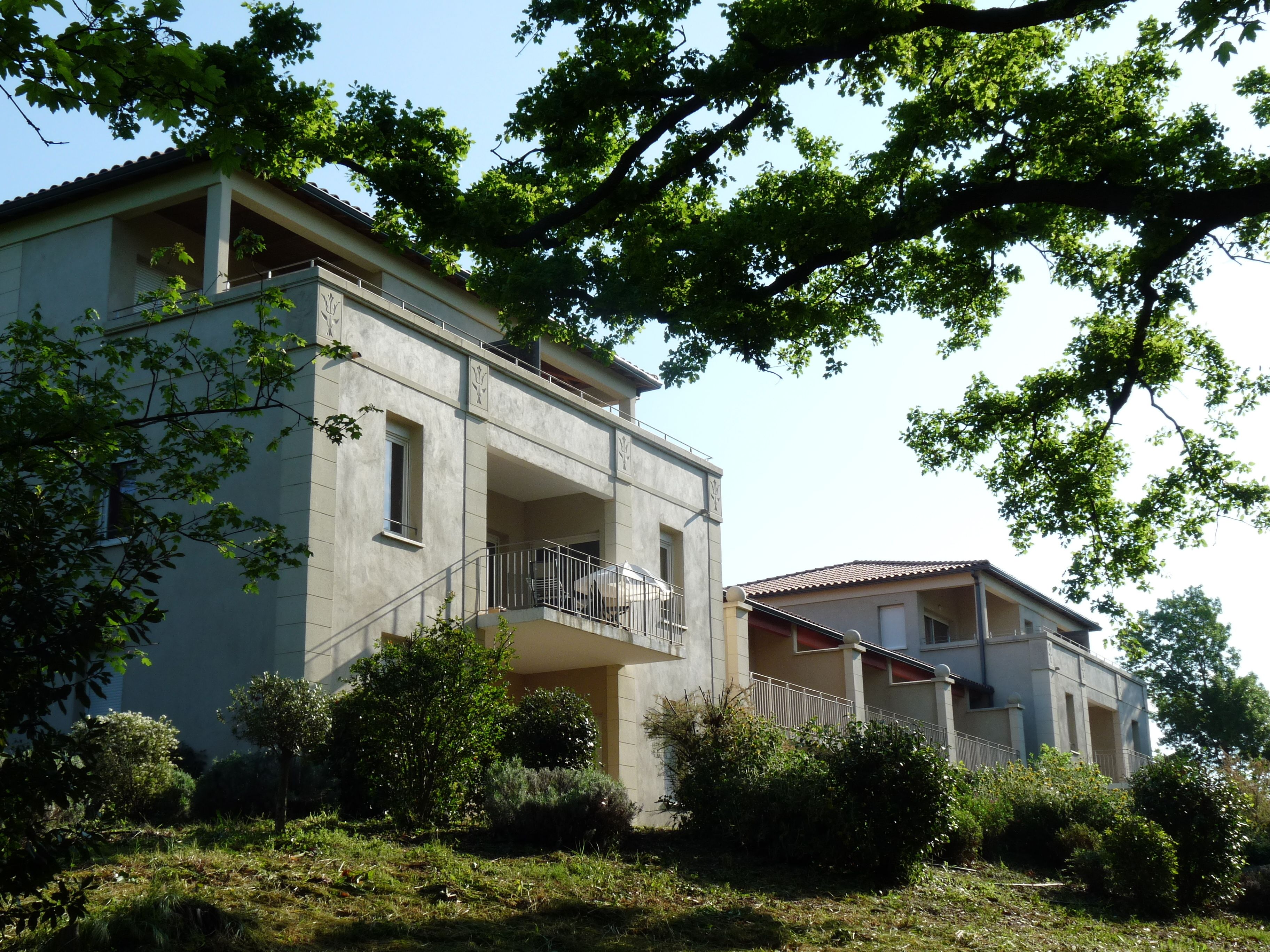 A two-story building with a balcony, surrounded by greenery and trees.