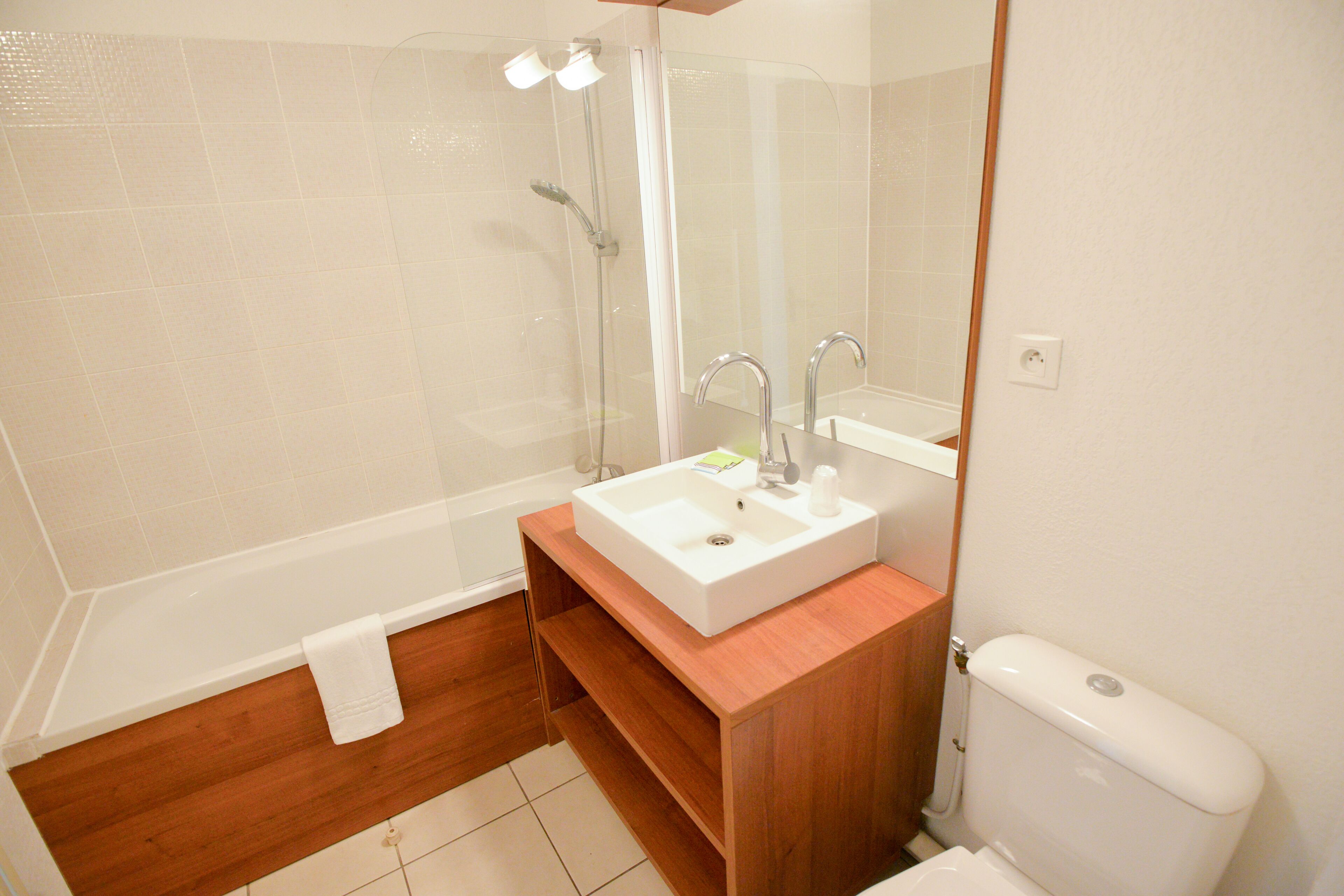 Un baño con una bañera blanca, ducha con cerramiento de vidrio, tocador de madera con lavamanos y un inodoro.