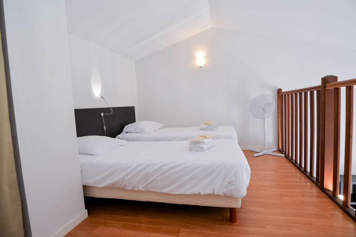 A bedroom with two beds, a ceiling fan, and a wooden railing.