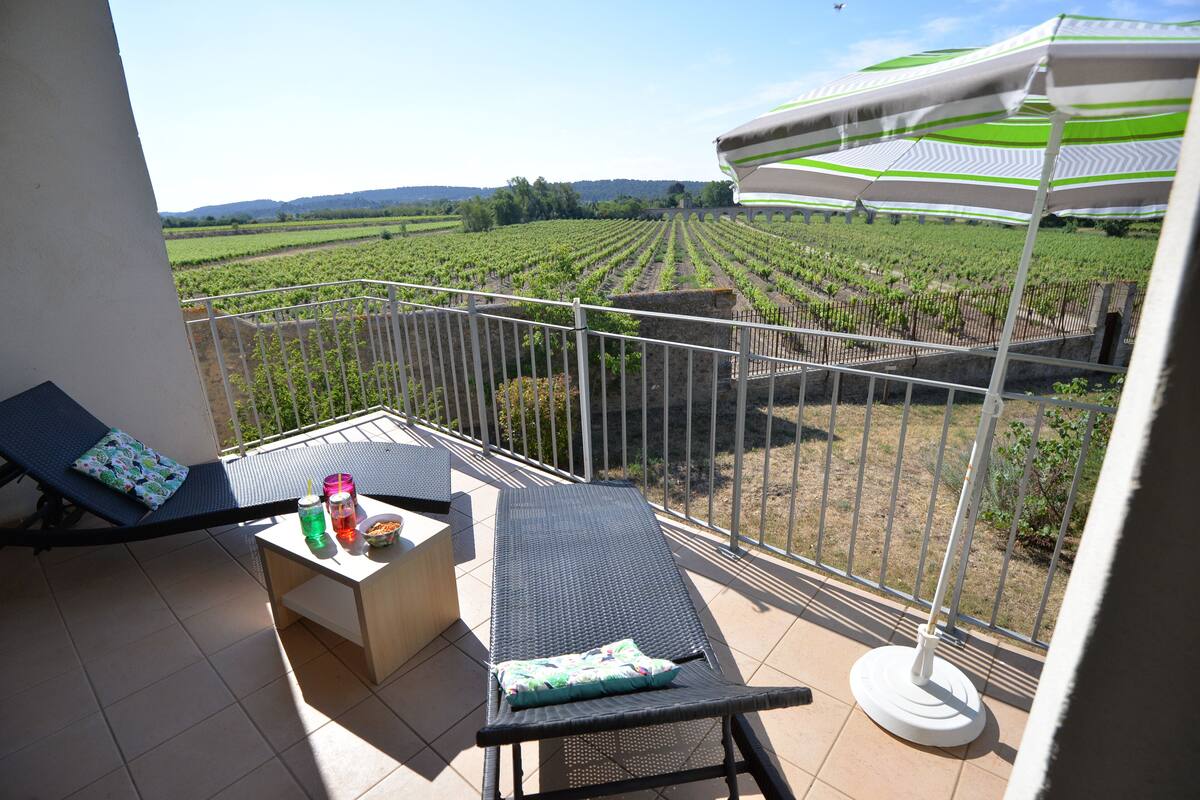 A balcony with two lounge chairs, a small table with drinks, and a view of a vineyard.