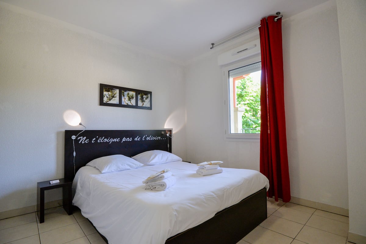 A neatly made bed with white linens, a dark headboard, and a small bedside table with a lamp.