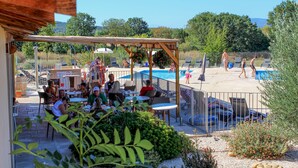 Zona de piscina al aire libre con sillones de descanso y sombrillas, rodeada de vegetación y un cielo despejado.