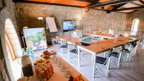 Un salón de conferencias con paredes de piedra, una mesa larga, sillas plegables, un ordenador portátil y una televisión.