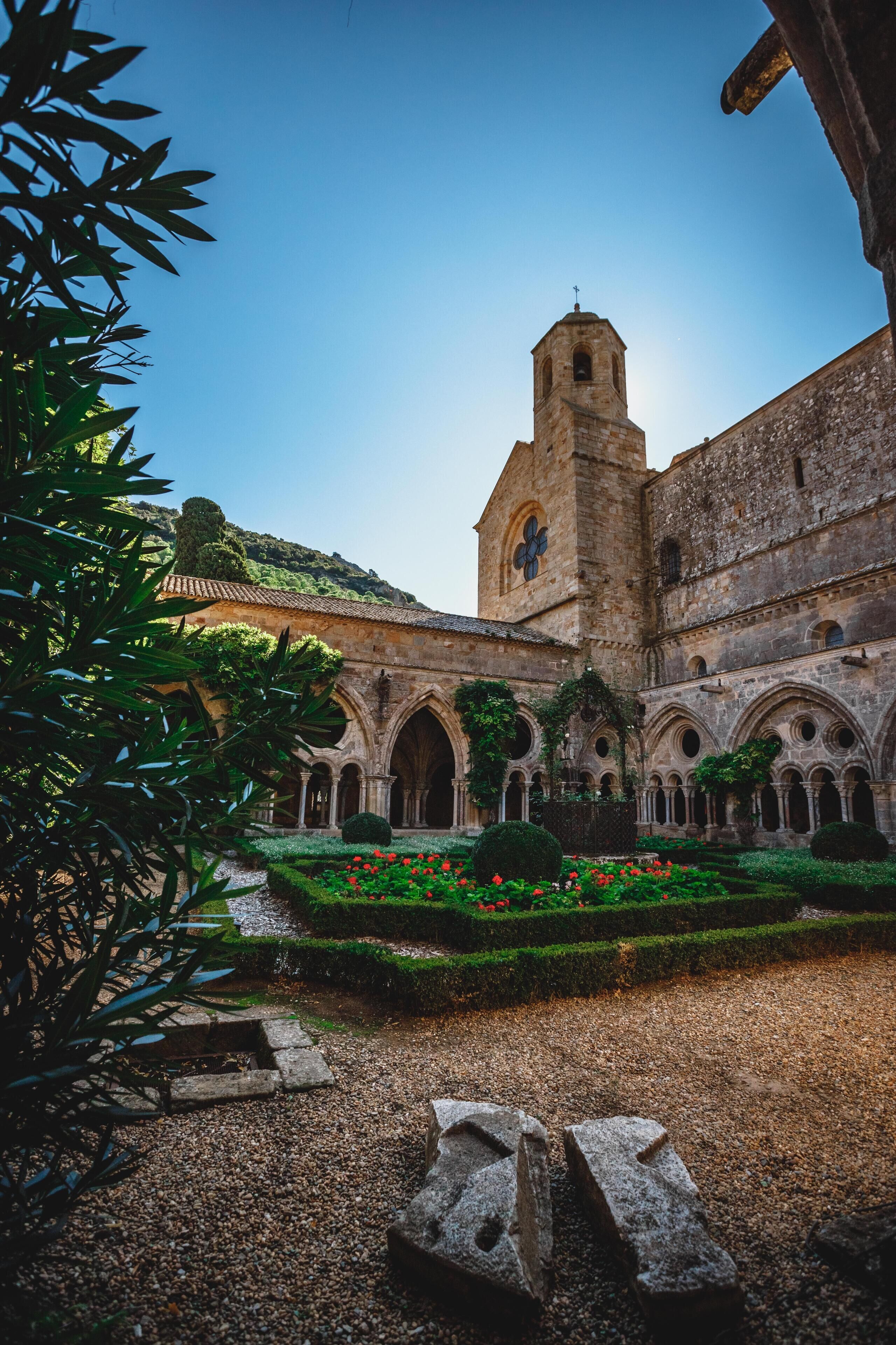 Un bâtiment historique doté d’une tour imposante, d’arcades et d’un jardin bien entretenu agrémenté de fleurs rouges.