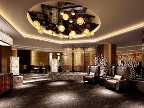 Un hall d’entrée moderne doté d’un espace salon central, d’un plafond haut orné d’un luminaire original et de panneaux muraux décoratifs.