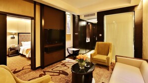 Habitación de hotel con cama, televisor, sofá, mesa de centro y una silla.
