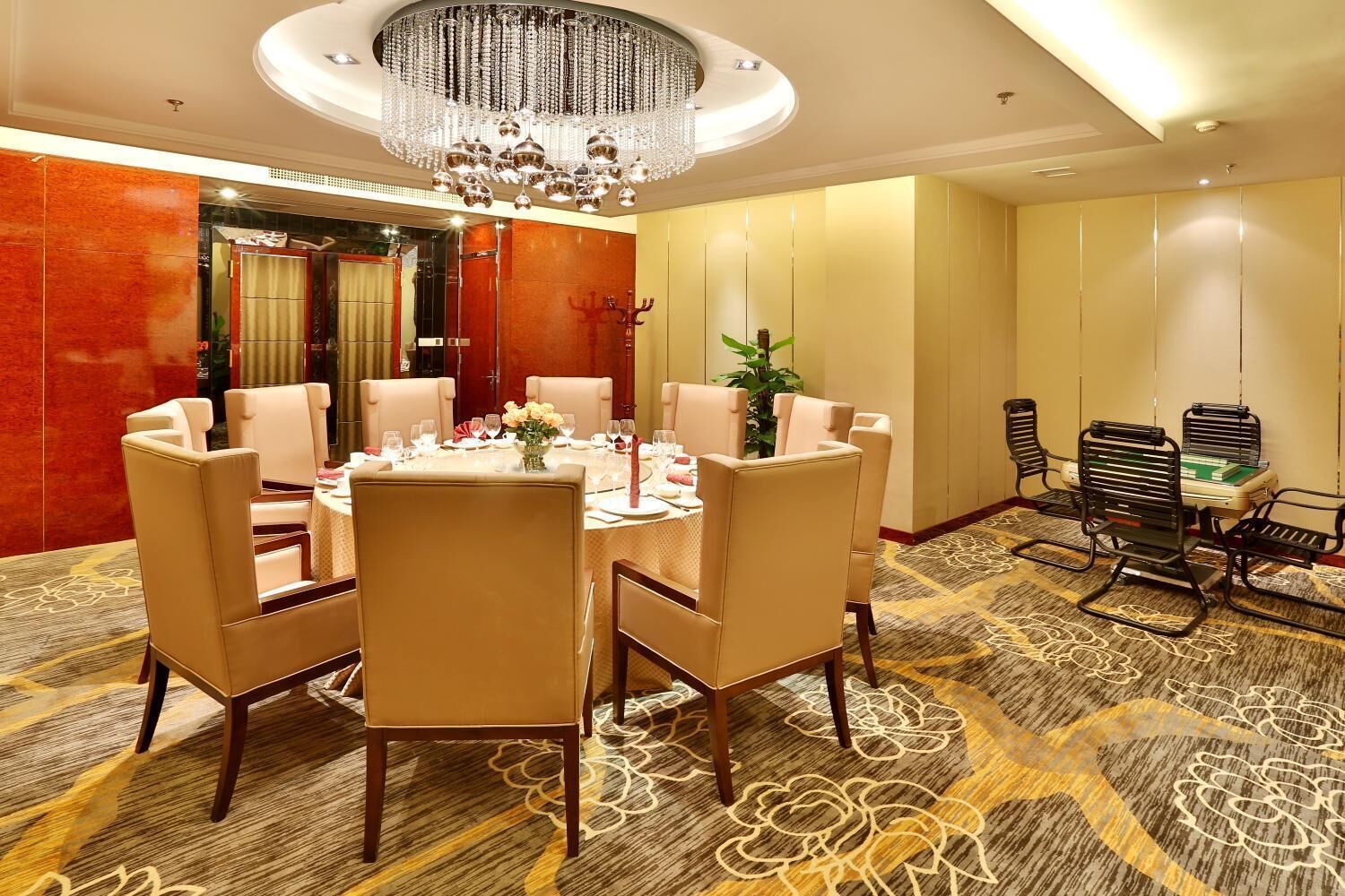 A conference room with a round table, beige chairs, a chandelier, and a carpeted floor.