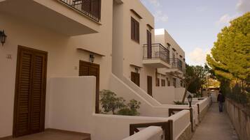 Un edificio residencial con varios balcones, contraventanas de madera y un camino pavimentado.